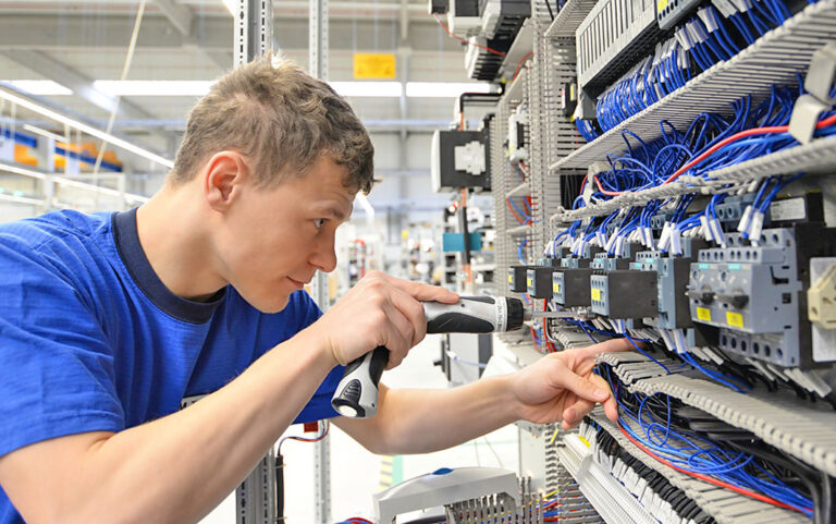 Elektrotechniker installiert die einzelnen Bestandteile eines Schaltschrankes in einer größeren Produktionshalle