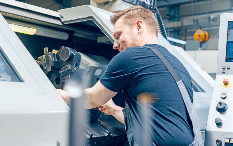 Ein Mitarbeiter einer Metall verarbeitenden Firma steht an einer modernen CNC-Fräse und wechselt das Fräswerkzeug. Die Rüstzeit wird dabei durch die Software planeus erfasst.